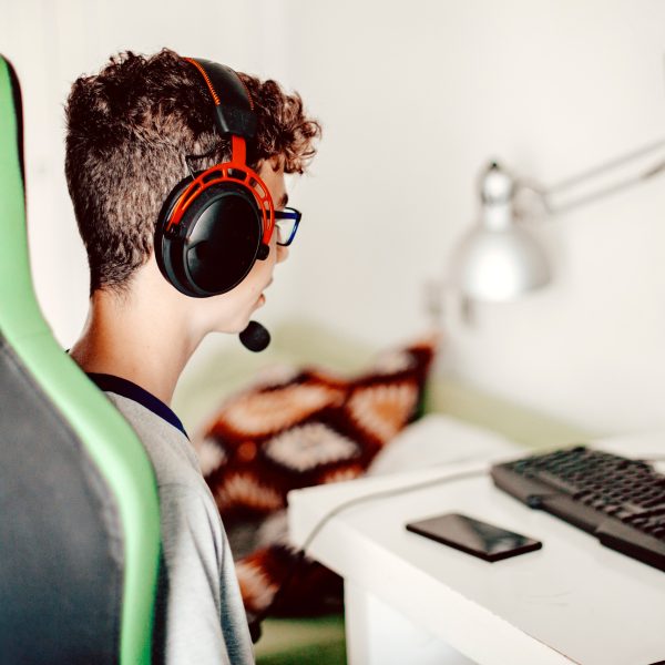 Eine Person in einem Gaming-Stuhl sitzt mit Headset auf dem Kopf vor einem Rechner.