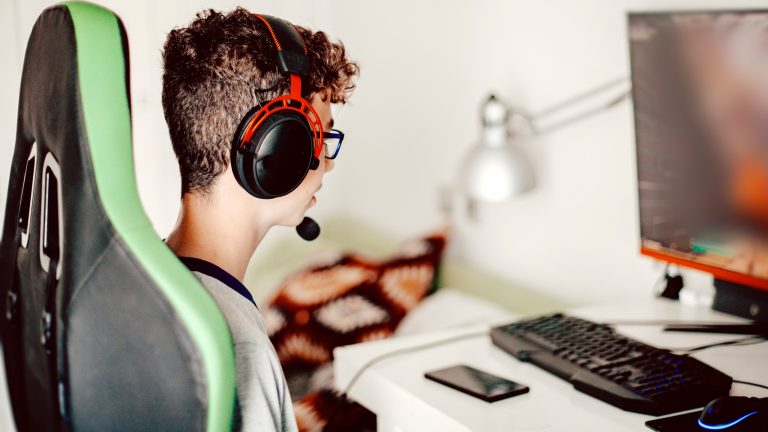 Eine Person in einem Gaming-Stuhl sitzt mit Headset auf dem Kopf vor einem Rechner.