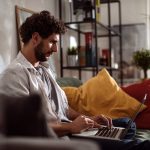 Eine Person sitzt mit einem MacBook auf dem Sofa.