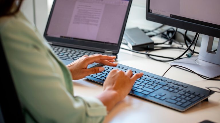 Eine Person sitzt an einem Schreibtisch und tippt an einer Tastatur.