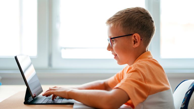 Ein Kind sitzt vor einem Tablet mit angedockter Tastatur und tippt darauf.