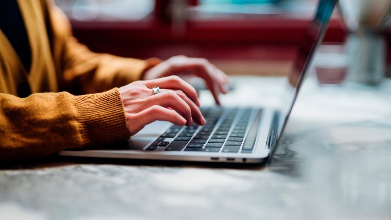 Eine Person sitzt vor einem MacBook und tippt mit zehn Fingern auf dessen Tastatur.
