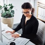 Eine Person sitzt an einem B&uuml;roschreibtisch und hat beide H&auml;nde auf einer Tastatur liegen.
