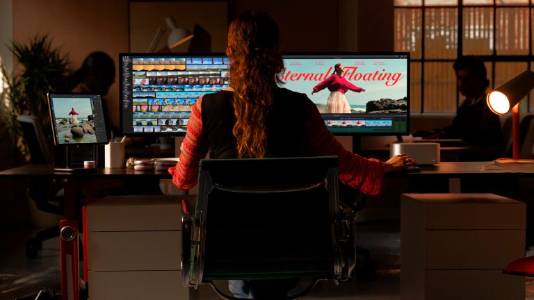 Eine Person sitzt an einem Schreibtisch und arbeitet auf zwei an einen Mac Studio angeschlossenen Monitoren.