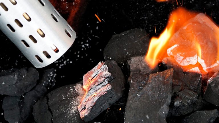 Nahaufnahme brennender Holzkohle, die von einem Grillgebläse angefacht wird.