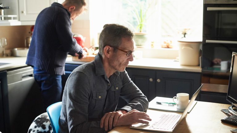 Eine Person sitzt in einer K&uuml;che an einem Tisch und bedient einen Laptop.