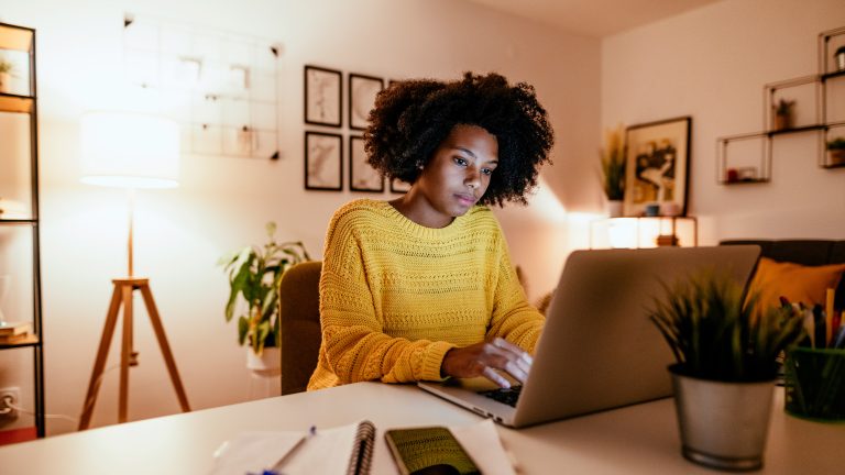 Eine Person sitzt an einem Schreibtisch und tippt auf der Tastatur eines MacBooks.