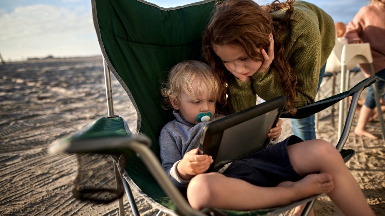 Zwei Kinder sind am Strand und schauen zusammen in ein Tablet.