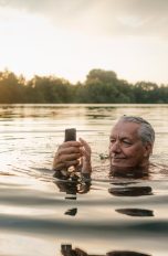 Eine Person schwimmt in einem See und bedient dabei ein Smartphone.