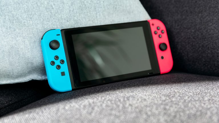 Eine Nintendo Switch steht an ein Kissen gelehnt auf einem Sofa.