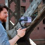 Eine Person h&auml;lt einen Gimbal in der Hand, in den ein iPhone 12 eingesetzt ist.