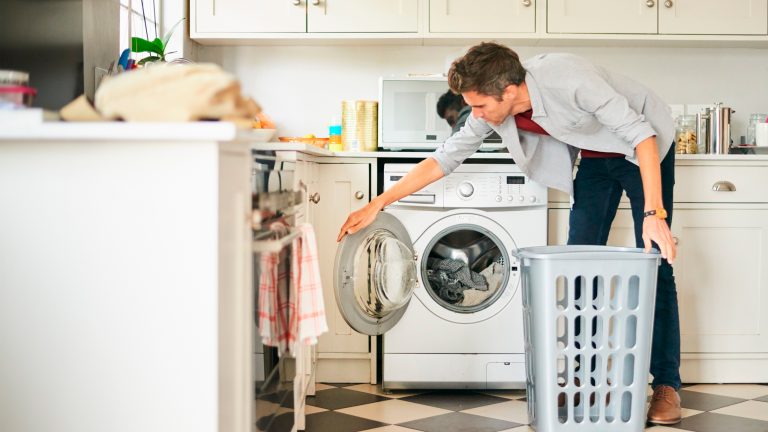 Eine Person hat Wäsche in eine Waschmaschine gefüllt und schließt nun die Trommel.