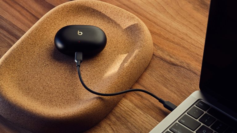 Ein Ladecase der Beats Studio Buds + ist per Kabel mit einem MacBook verbunden. Am Ladecase weist eine rot leuchtende LED auf den Ladevorgang hin.