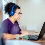 Eine Person mit Kopfh&ouml;rern sitzt vor einem Laptop.