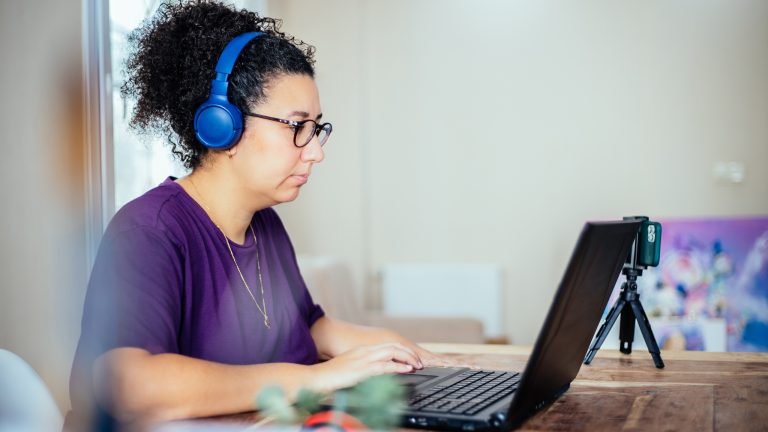 Eine Person mit Kopfhörern sitzt vor einem Laptop.