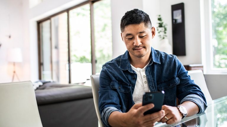 Eine Person mit einem Smartphone in der Hand sitzt an einem Glastisch.