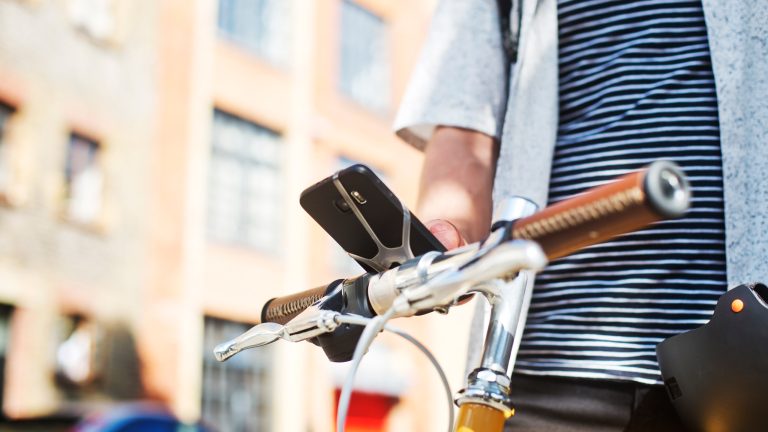 Eine Person hat ihr Smartphone per Halterung am Lenker eines Fahrrads angebracht und bedient das Gerät.