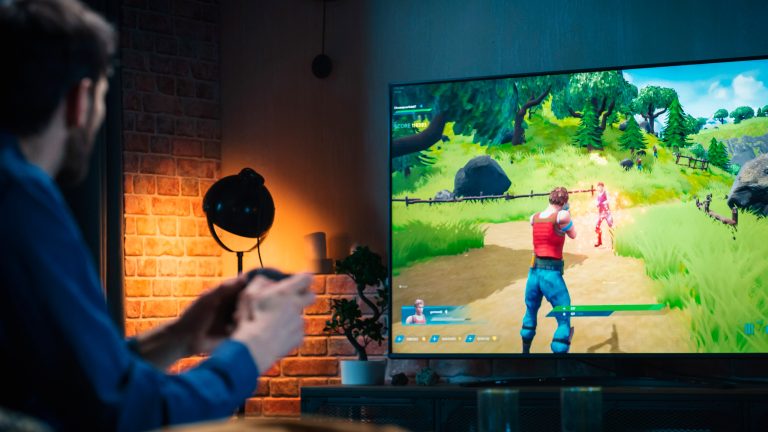 Eine Person sitzt vor einem Fernseher und spielt auf einer angeschlossenen Konsole.