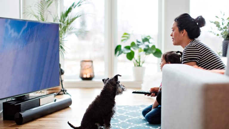 Eine Person sitzt mit einem Kind vor einem Fernseher, der auf dem Boden steht.