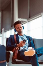 Eine Person sitzt im Wartebereich eines Flughafens und hört über Kopfhörer Musik.