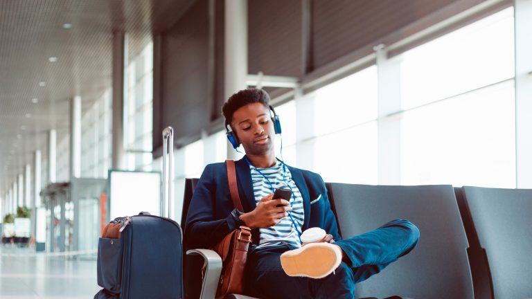 Eine Person sitzt im Wartebereich eines Flughafens und hört über Kopfhörer Musik.