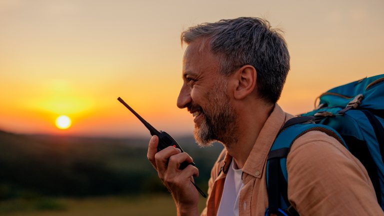 Eine Person mit Wanderrucksack spricht in einen Walkie-Talkie.