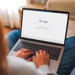 Eine Person hat einen Mac, auf dem die Google-Website geöffnet ist, auf dem Schoß.