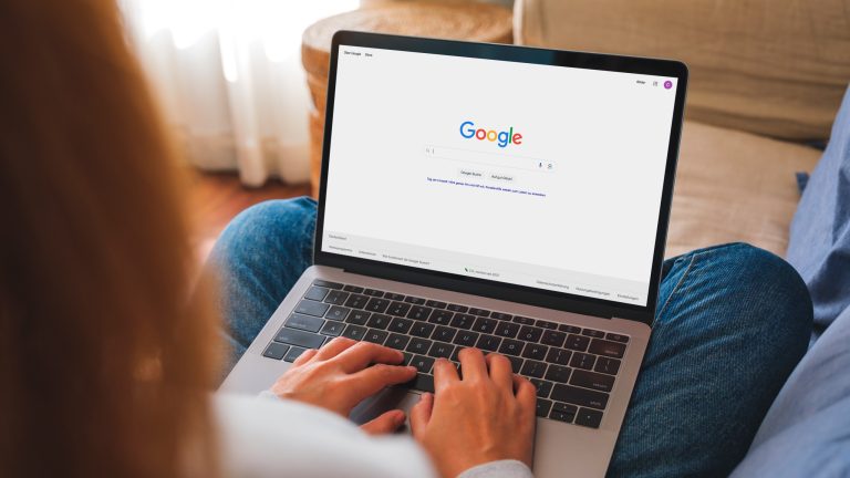 Eine Person hat einen Mac, auf dem die Google-Website geöffnet ist, auf dem Schoß.