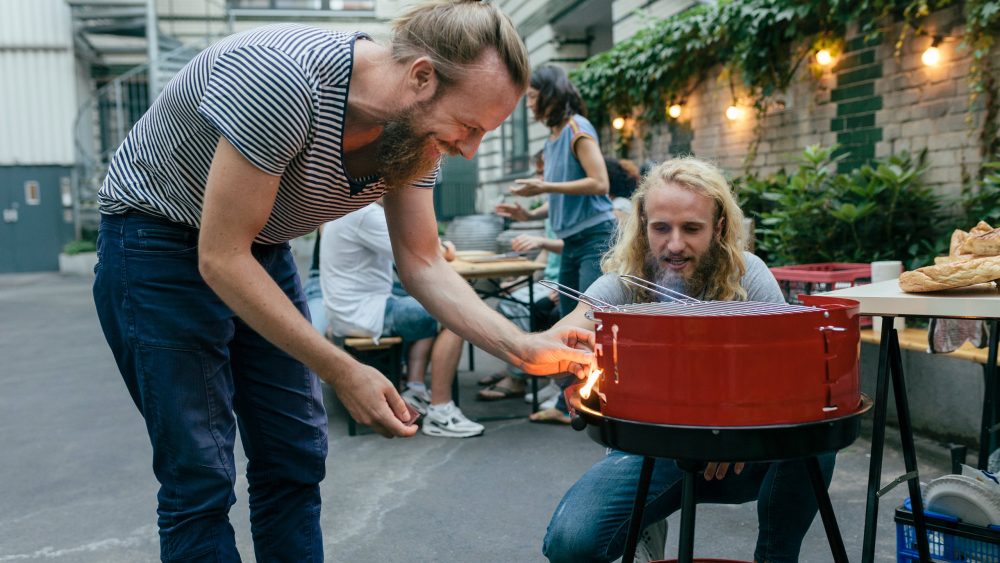 Zwei Personen stehen um einen Grill und entz&uuml;nden diesen.
