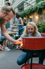 Zwei Personen stehen um einen Grill und entz&uuml;nden diesen.