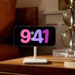 Ein iPhone 14 Pro hängt im Querformat auf einer Ladestation auf einem Nachttisch und zeigt die Uhrzeit an.