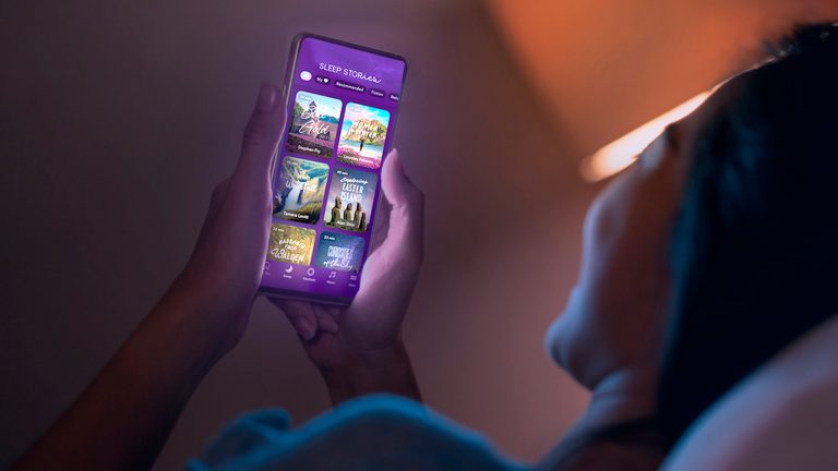 Eine Person liegt im Bett und schaut auf die Calm-App auf ihrem Handy.