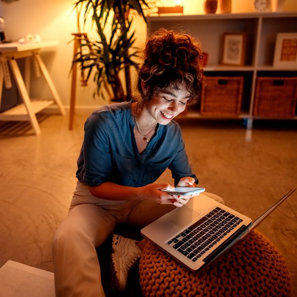 Eine Person sitzt mit einem iPhone in der Hand vor einem MacBook Pro.