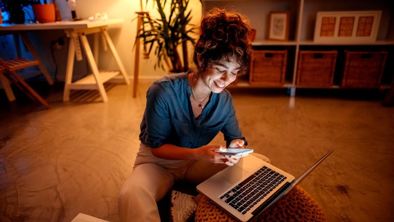 Eine Person sitzt mit einem iPhone in der Hand vor einem MacBook Pro.