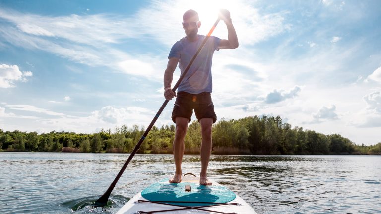Eine Person steht auf einem Stand-up Paddle Board und paddelt durch einen See.