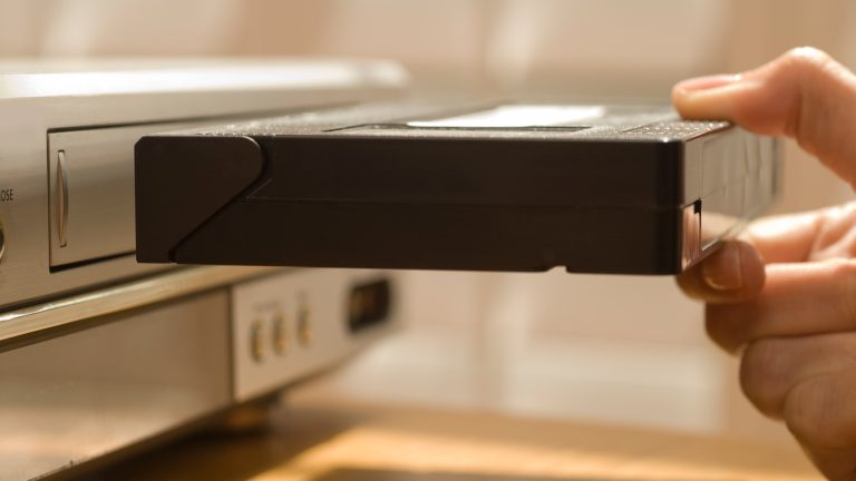 Eine Person schiebt eine VHS-Kassette in einen VHS-Player.