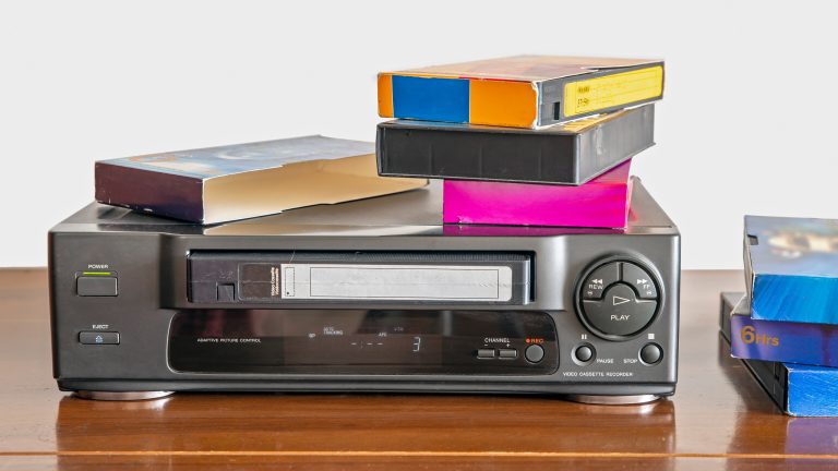 Ein VHS-Player auf einem Schrank. Auf dem Gerät liegen einige VHS-Kassetten.
