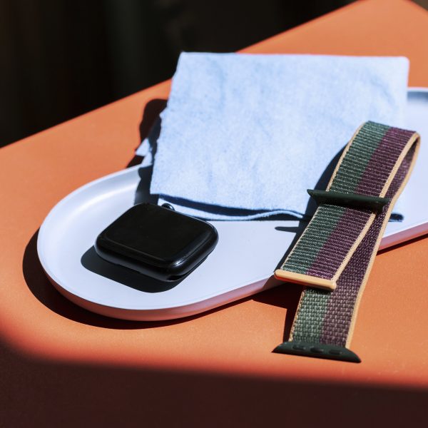 Eine auseinandergebaute Apple Watch liegt neben einem Putztuch in einer hellblauen Schale.
