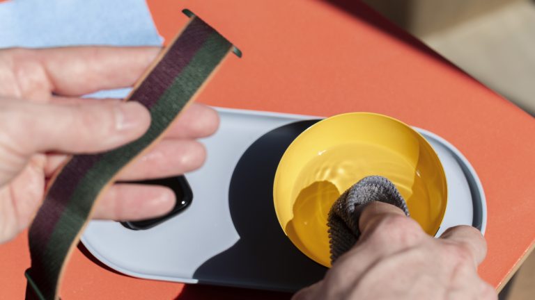 Eine Person feuchtet mit der rechten Hand ein Mikrofasertuch an, in der linken h&auml;lt er ein Armband der Apple Watch.
