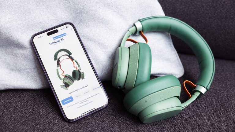 Fairbuds XL in Gr&uuml;n liegen neben einem iPhone, auf dem die Explosionsansicht in der App zu sehen ist.