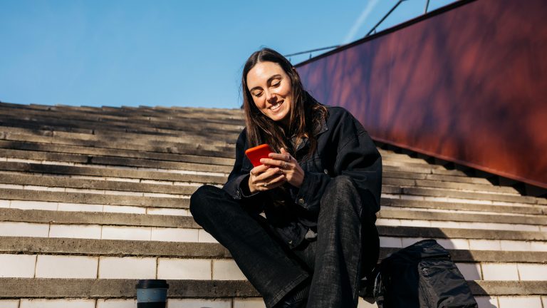 Eine Person sitzt auf einer Freilichttreppe und schaut auf ein Smartphone.