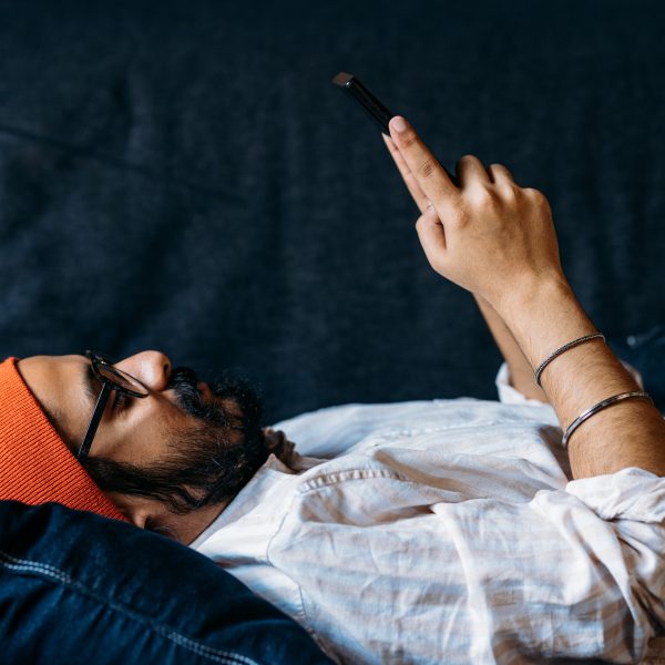 Eine Person liegt auf einem Sofa und schaut auf das Smartphone in ihren H&auml;nden.