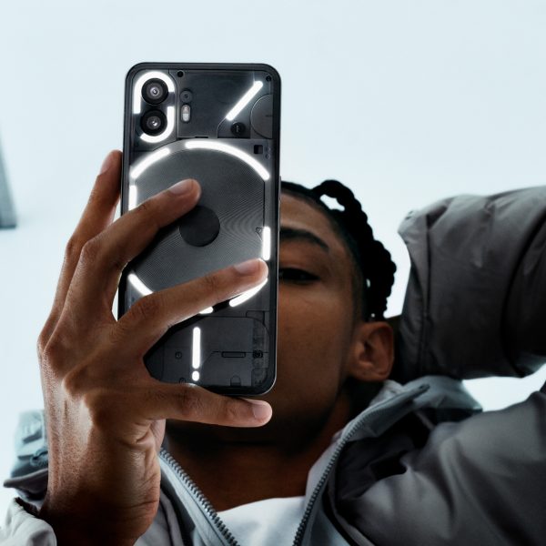 Eine Person h&auml;lt ein Nothing Phone (2) in der Hand, dessen R&uuml;ckseite durch das Glyph Interface illuminiert ist.