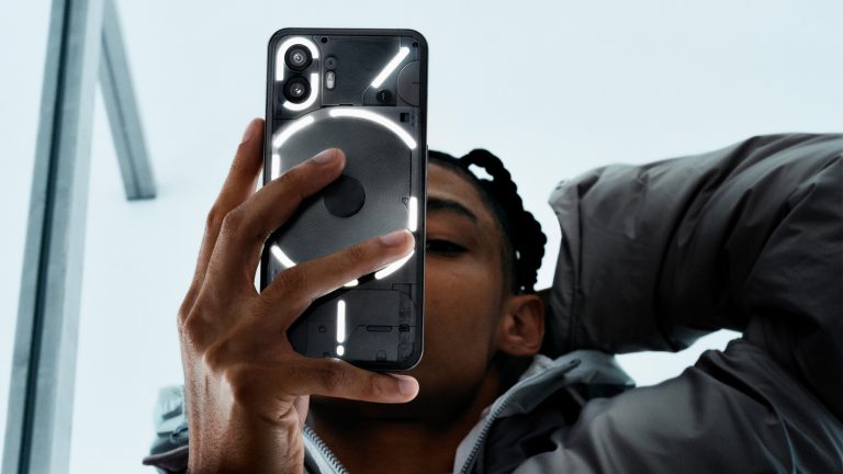 Eine Person hält ein Nothing Phone (2) in der Hand, dessen Rückseite durch das Glyph Interface illuminiert ist.