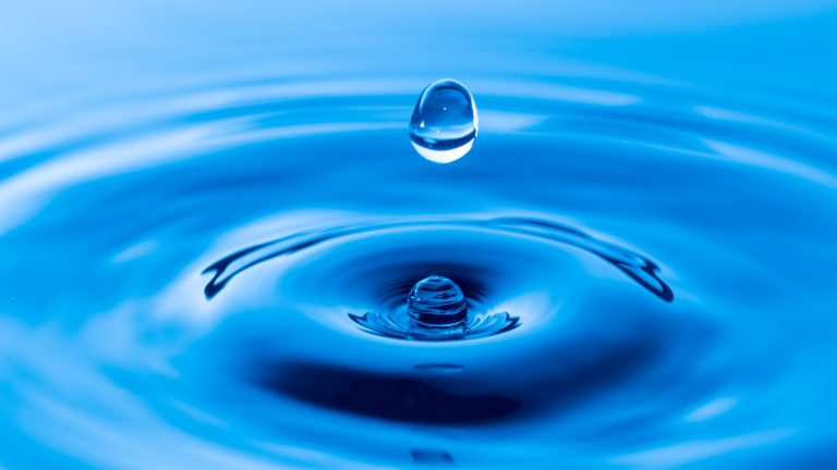 Ein Wassertropfen scheint über einer Wasseroberfläche zu schweben.