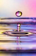 Nahaufnahme eines Wassertropfens, der von einer mit Wasser bedeckten Oberfl&auml;che nach oben prallt.