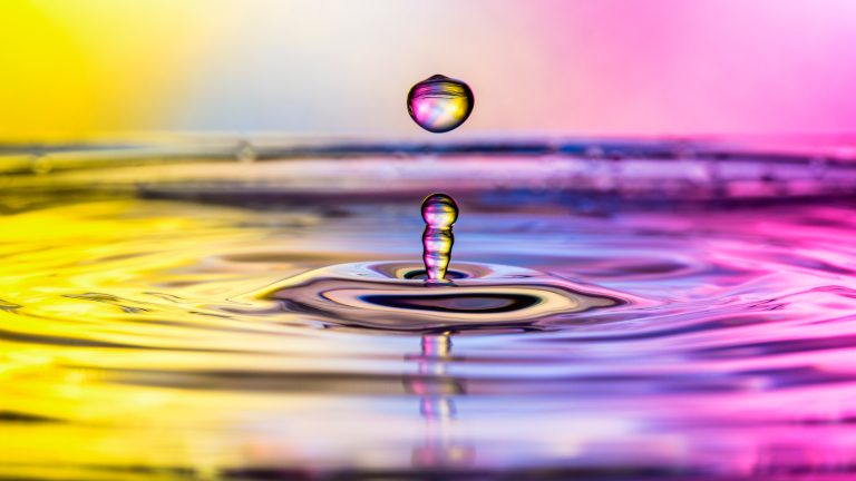 Nahaufnahme eines Wassertropfens, der von einer mit Wasser bedeckten Oberfläche nach oben prallt.