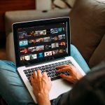 Eine Person sitzt vor einem Laptop. Auf dem Bildschirm ist das Hauptmen&uuml; von Netflix zu sehen.