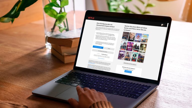 Eine Person sitzt vor einem Laptop auf einem Tisch. Zu sehen ist die Kündigungsseite von Netflix.