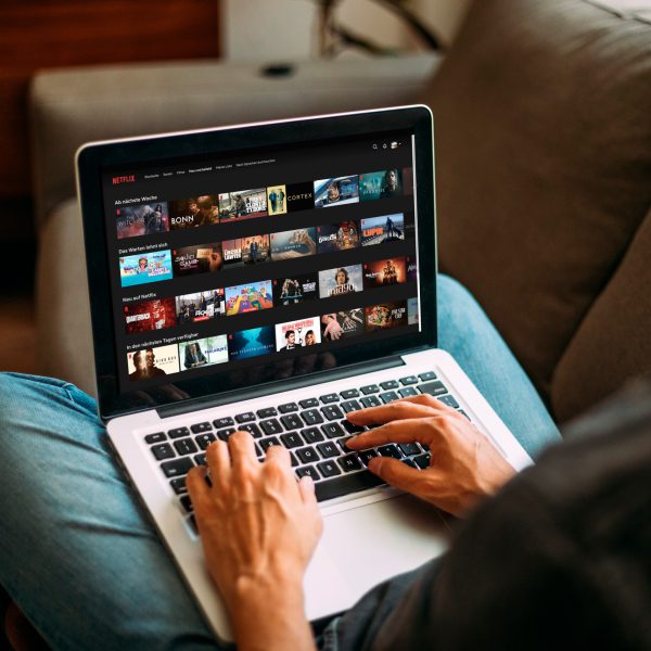 Eine Person sitzt vor einem Laptop. Auf dem Bildschirm ist das Hauptmen&uuml; von Netflix zu sehen.